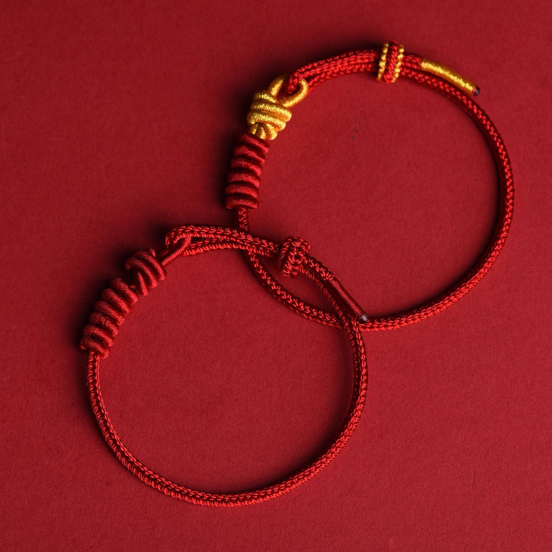 Close up view of a handmade red string eight stranded rope bracelet with gold tone knots on a red background