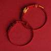 Close up view of a handmade red string eight stranded rope bracelet with gold tone knots on a red background