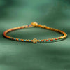 Close-up of a thin multicolor braided rope bracelet with a small gold coin charm on a green background