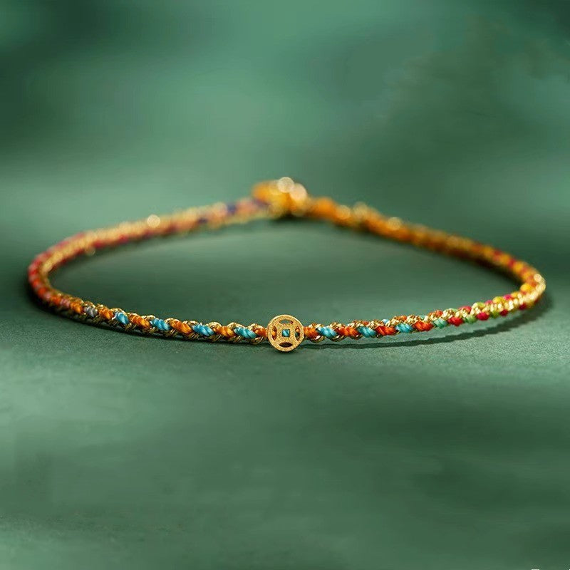 Close-up of a thin multicolor braided rope bracelet with a small gold coin charm on a green background