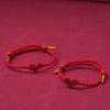 Two hand-woven red string bracelets with sheep knots and gold tips on a maroon background