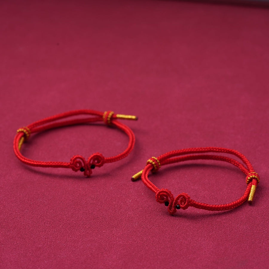 Two hand-woven red string bracelets with sheep knots and gold tips on a maroon background