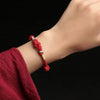 Close up of a red braided bracelet with a central knot and jade beads on a wrist