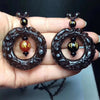 Hand holding two dark obsidian ring pendants with carved animals and central mantra beads