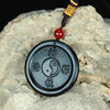 Close up of a black round jade pendant with a Yin Yang symbol and Chinese characters on a rock.