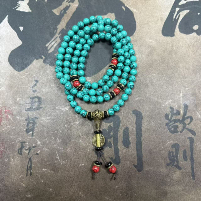 Coiled string of turquoise beads with red accents and a guru bead resting on a textured surface.