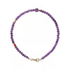 A delicate bracelet made of small purple amethyst beads with gold-tone spacers lying on a light surface