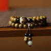 A close up of a green sandalwood double wrap bracelet with a carved lotus bead on a wooden surface.