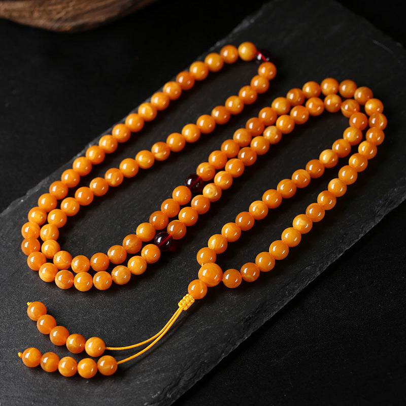Coiled natural amber round bead mala necklace with yellow tassel on dark slate background