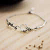 Silver copper bracelet with a white chalcedony stone and dark plum blossom accents on a wooden surface.