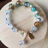 Light blue chalcedony beaded bracelet with glass accents and flower charm on wooden display