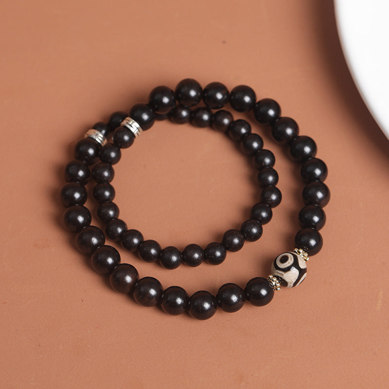 Close up of black wood beads and a patterned Dzi bead on a bracelet