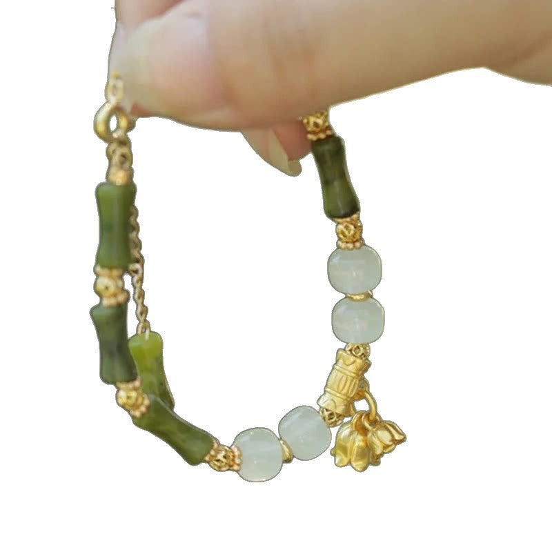 Hand holding a bracelet with green bamboo beads and white jade stones