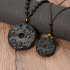 Two round black obsidian pendants with dragon and phoenix carvings resting on grey fabric