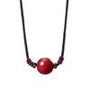 Red cinnabar bead pendant on a black string necklace with colorful accents
