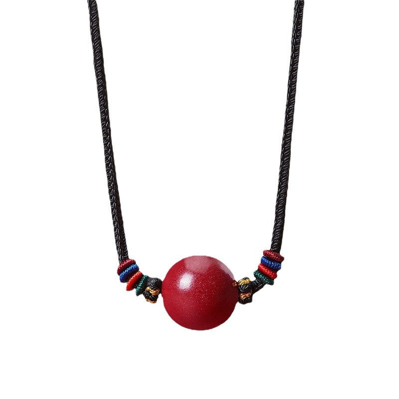 Red cinnabar bead pendant on a black string necklace with colorful accents