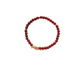 Close up of red cinnabar bead bracelet with small gold-tone koi fish charm on white background