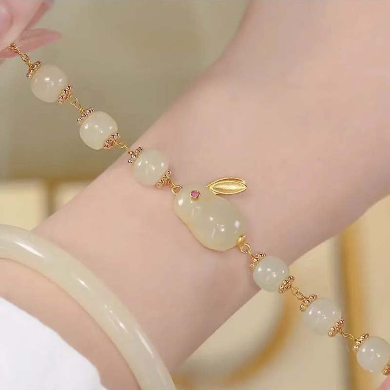 Close-up of a wrist wearing a beaded bracelet with a white rabbit charm and gold accents