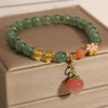 Green strawberry quartz beaded bracelet with a pink peach charm and gold flower accent on a box