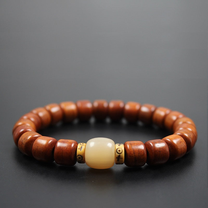 Close-up of a wooden bead bracelet with a cream-colored bone center bead and gold-tone spacers on a dark background