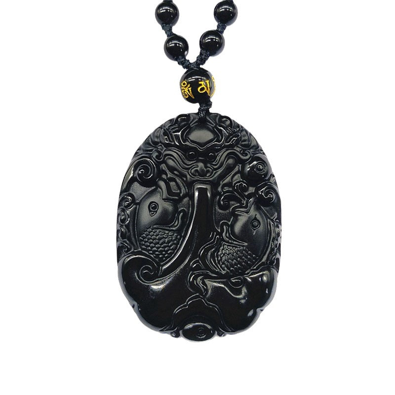 Hand holding a polished black obsidian pendant carved with two koi fish