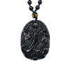Hand holding a polished black obsidian pendant carved with two koi fish