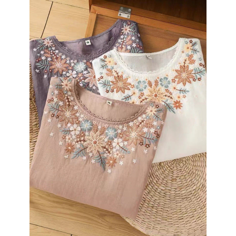 Three folded cotton linen tops with floral embroidery on a wooden surface