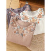 Three folded cotton linen tops with floral embroidery on a wooden surface