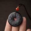 Close-up of a black glass peace buckle pendant with carved mantras held in hand