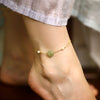 Close up of a gold tone anklet with a green jade peace buckle worn on an ankle