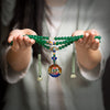 Hands holding a green agate 108 bead mala necklace with a colorful round pendant