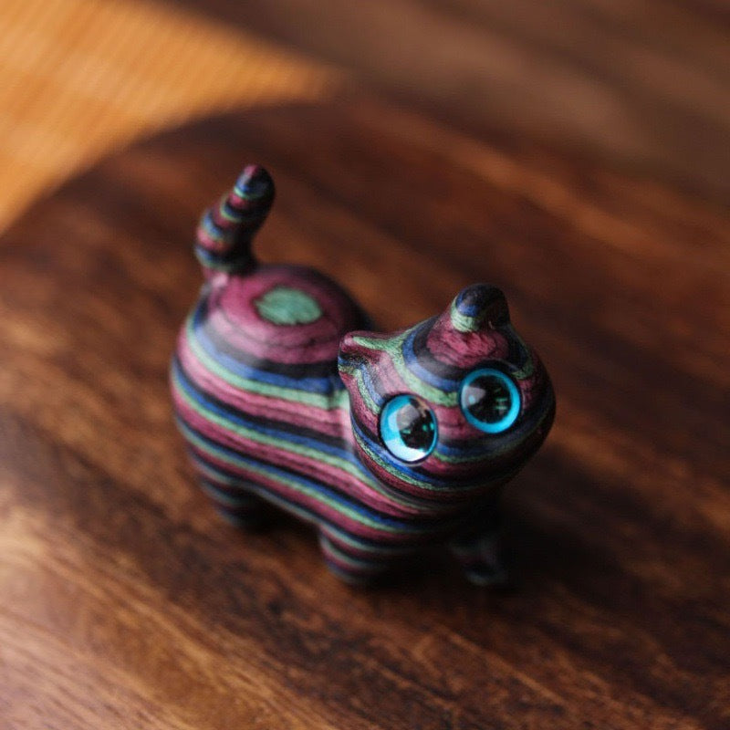 Close-up view of a colorful striped wooden cat figurine with blue eyes on a wooden surface