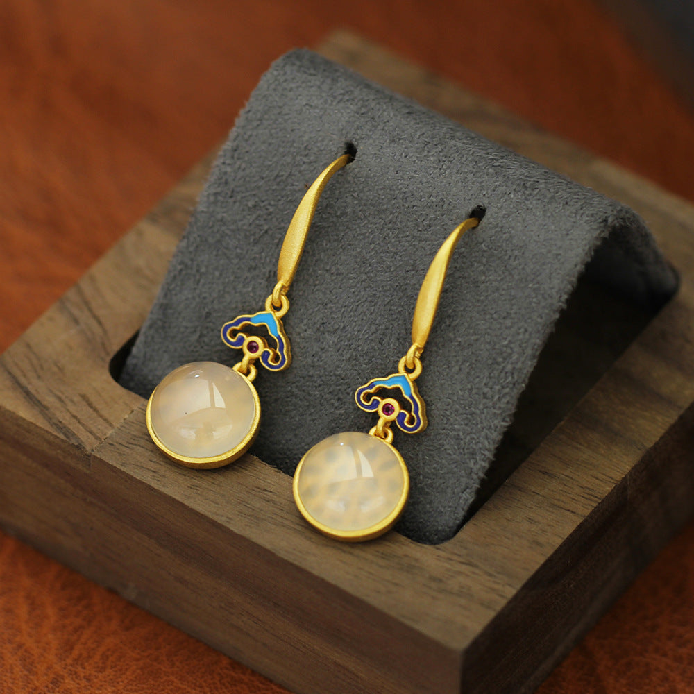 Pair of gold-tone drop earrings with blue enamel clouds and faux jade stones on a grey stand