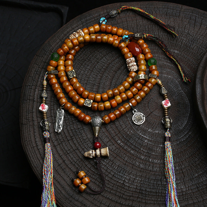 Close up of 108 bead yak bone mala necklace with copper accents and tassels on wood surface