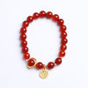 Red cinnabar beaded bracelet with gold-tone Fu charm on a white surface