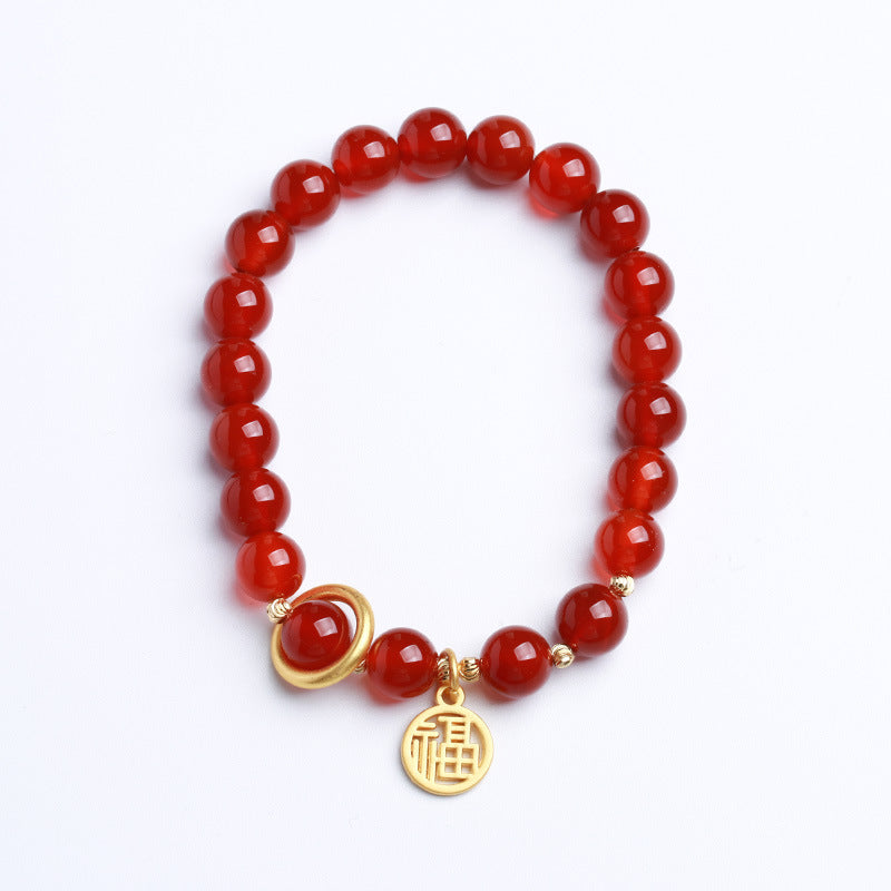 Red cinnabar beaded bracelet with gold-tone Fu charm on a white surface