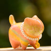 Close-up of a glossy pink and yellow lacquered wooden cat figurine wearing a pearl necklace