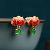 Close-up of red enamel lotus flower earrings with green stone drops on a blue bowl rim
