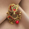 Gold-tone dragon brooch with red accents and a red pearl on fabric