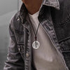Man wearing a vintage silver-tone copper coin pendant on a black cord.