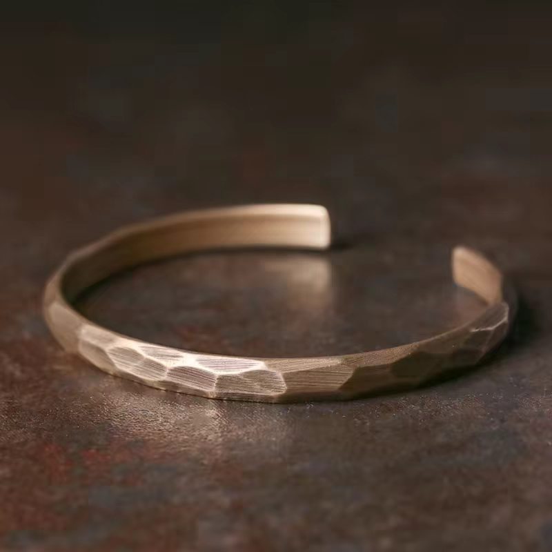 Close up of a bronze colored geometric steel cuff bracelet on a dark surface