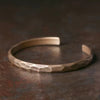 Close up of a bronze colored geometric steel cuff bracelet on a dark surface