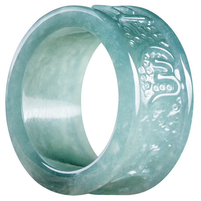 Close up of a light green jade ring with carved mantras resting on wood