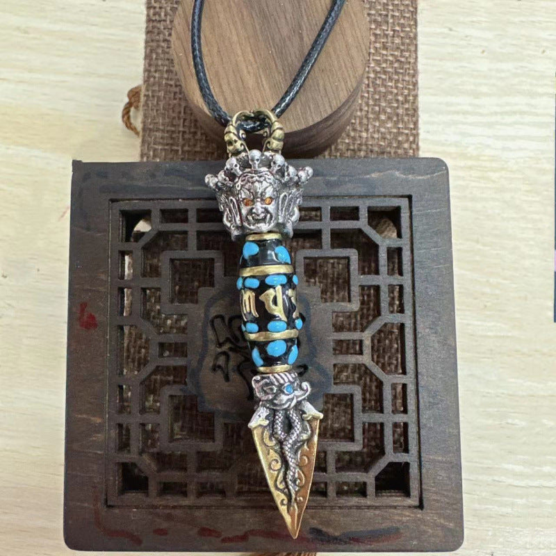 Copper phurba pendant necklace with a rotating blue dzi bead, resting on brown paper.