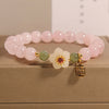 Pink rose quartz beaded bracelet with a white flower and gold charm on a box