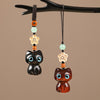 Two wooden cat charms hanging from a branch, one dark ebony and one reddish purple sandalwood.