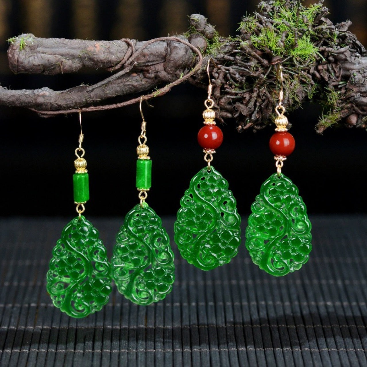 Green carved jade drop earrings hanging from a branch