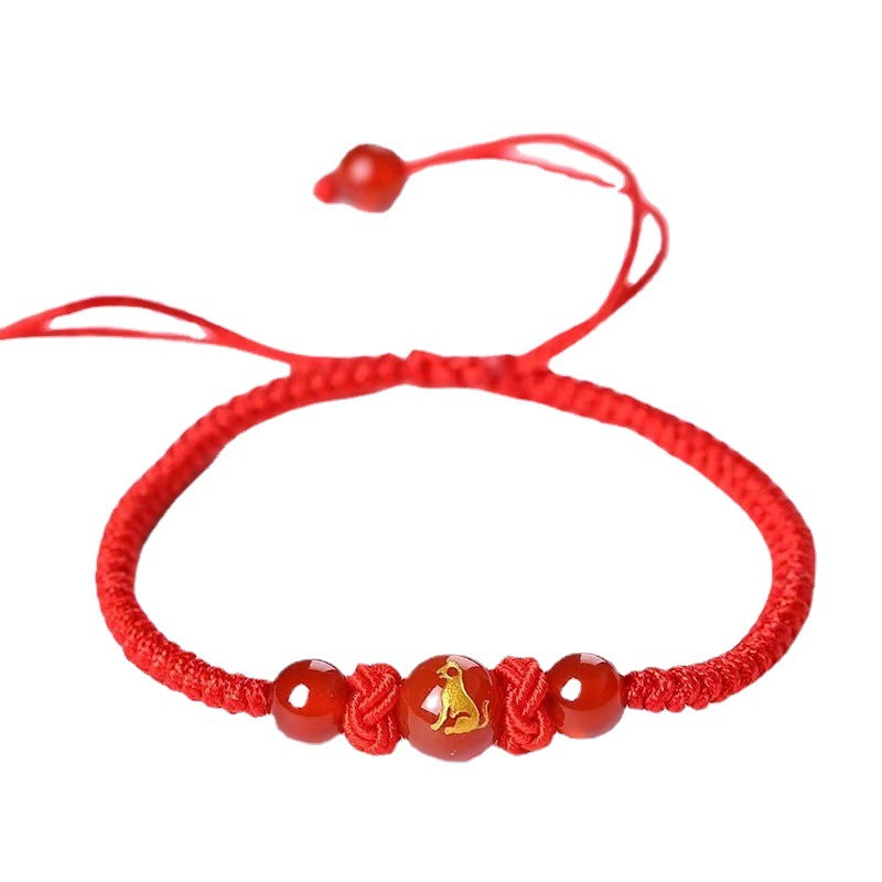 Close-up of a red braided bracelet with agate beads and a gold zodiac charm on a white surface