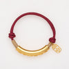 Close up of a braided red cord bracelet with a gold curved charm on a wrist