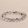 A close up view of a clear bead bracelet with internal sparkles on a beige background